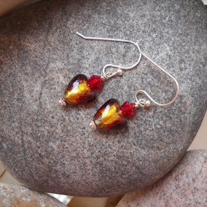 May include: A pair of silver earrings with red and gold heart-shaped glass beads. The beads have a metallic finish and are accented with small red crystal beads.