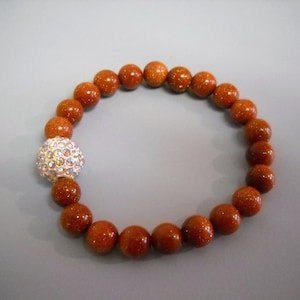 May include: A brown beaded bracelet with a sparkly silver ball charm.