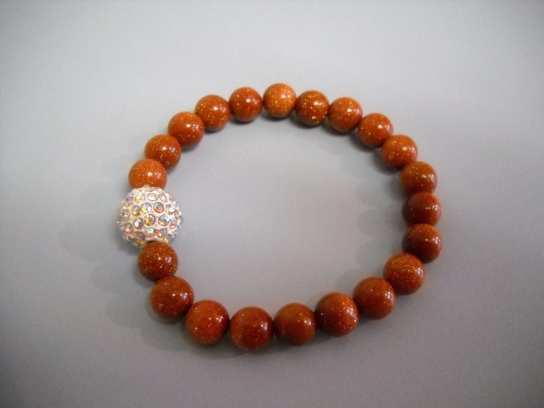 May include: A brown beaded bracelet with a sparkly silver ball charm.