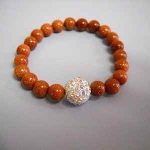 May include: A brown beaded bracelet with a sparkly silver ball charm.