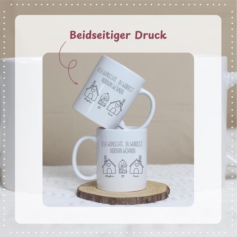 Puede incluir: Dos tazas de cer&aacute;mica blanca apiladas sobre un posavasos de madera. Cada taza presenta un dibujo lineal negro de casas y el texto "ICH WUNSCHTE, DU WURDEST NEBINAN WOHNEN". Las tazas tienen un asa en el lado derecho.