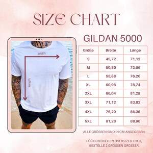 May include: A white Gildan 5000 t-shirt is displayed on a person, with a size chart showing measurements in centimeters. The chart includes sizes S to 5XL, with width and length measurements. The text "SIZE CHART" is at the top.