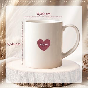 May include: A cream-colored ceramic mug with a heart-shaped design containing the text "330 ml". The mug is 3.74 inches tall and 3.15 inches wide. The mug has a curved handle and is displayed on a wooden surface.