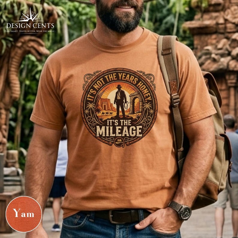 K&ouml;nnte beinhalten: Ein yamfarbenes T-Shirt mit einem kreisf&ouml;rmigen Grafikdesign, das eine Silhouette einer Person mit einer Peitsche zeigt, mit dem Text "IT'S NOT THE YEARS HONEY, IT'S THE MILEAGE". Das Shirt hat kurze &Auml;rmel und wird von einer Person getragen.