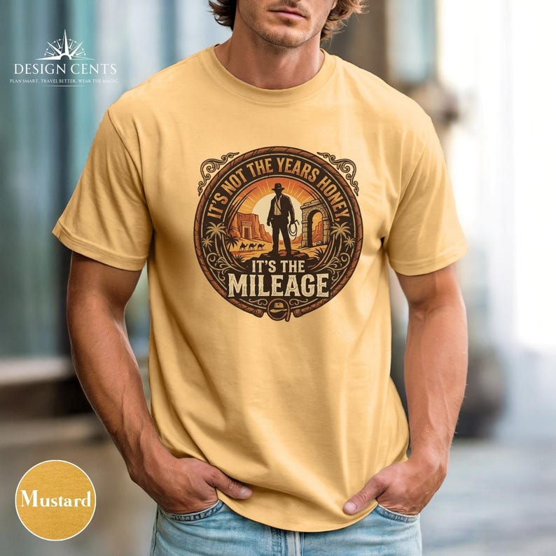 K&ouml;nnte beinhalten: Senffarbenes T-Shirt mit einem kreisf&ouml;rmigen Aufdruck mit dem Text "IT'S NOT THE YEARS HONEY IT'S THE MILEAGE". Die Grafik zeigt einen Cowboy in einer W&uuml;stenlandschaft. Das T-Shirt hat kurze &Auml;rmel und einen Rundhalsausschnitt.