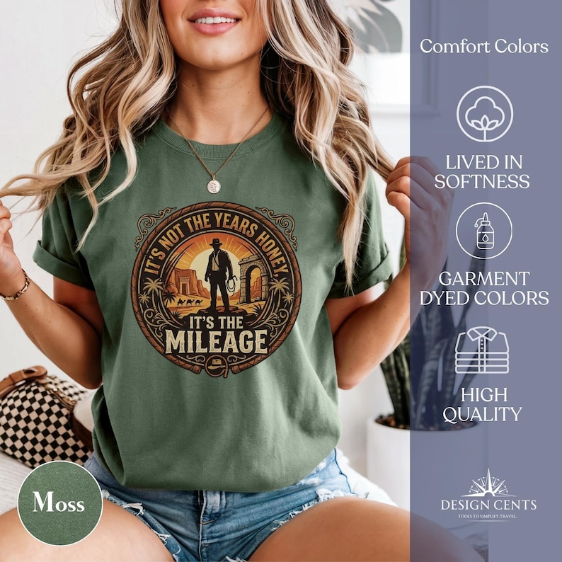K&ouml;nnte beinhalten: Ein moosgr&uuml;nes T-Shirt mit einem kreisf&ouml;rmigen Grafikdesign, das eine Silhouette einer Person mit einem Seil zeigt, mit dem Text "IT'S NOT THE YEARS HONEY, IT'S THE MILEAGE". Das Shirt hat hochgekrempelte &Auml;rmel und ist aus weichem Material.