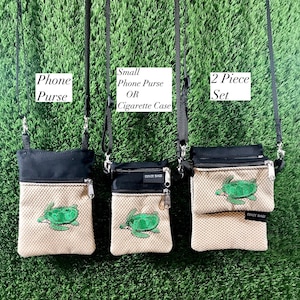 May include: Three small crossbody bags with black straps and zipper closures. The bags are made of a beige fabric with a woven texture and feature a green embroidered sea turtle design. The bags are labeled "Phone Purse", "Small Phone Purse OR Cigarette Case", and "2 Piece Set".