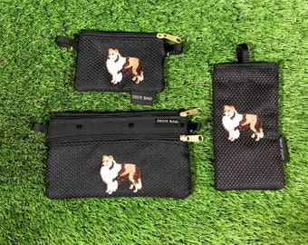 Op de afbeelding: Drie zwarte mesh-ritszakjes met geborduurde afbeeldingen van een bruine en witte hond. De zakjes hebben de tekst "Dixie Bags" erop gedrukt.