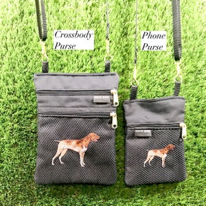 May include: Two black canvas crossbody purses with adjustable straps. The larger purse has the text "Crossbody Purse" above it and the smaller purse has the text "Phone Purse" above it. Both purses have a mesh pocket and a zippered pocket. Both purses have a brown and white dog embroidered on them. The text "Dixie Bags" is on the zippered pocket of both purses.