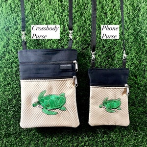 Puede incluir: Dos bolsos de bandolera negros y beige con un diseño de tortuga marina. El bolso más grande está etiquetado como "Crossbody Purse" y el bolso más pequeño está etiquetado como "Phone Purse".