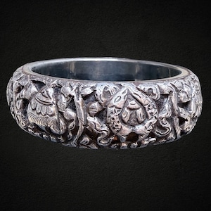 Brazalete tibetano repujado de plata con motivos florales, animales, tribales y étnicos sobre metal blanco, estilo vintage retro apilable.