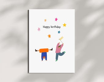 May include: A white greeting card with the words "Happy birthday" and colorful star illustrations. The card features two cartoon figures, one upside down and the other holding a flag, with a light shadow overlay.