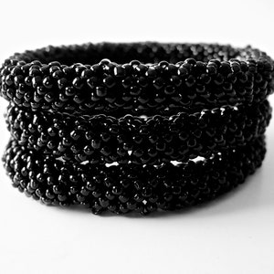May include: A stack of three black beaded bracelets. The bracelets are made of small, round beads that are tightly woven together.