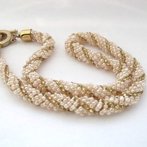 May include: A multi-strand necklace made of small white and gold beads woven together in a twisted pattern. The necklace has a gold clasp.