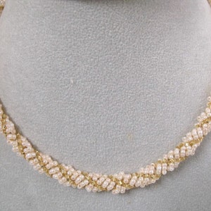 May include: A gold and white beaded necklace with a twisted design.
