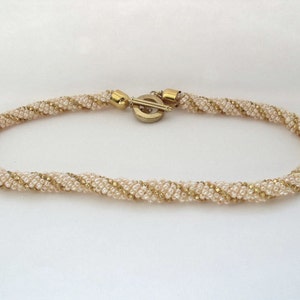 May include: A gold and cream beaded necklace with a twisted design. The necklace has a gold clasp.