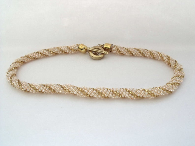 May include: A gold and cream beaded necklace with a twisted design. The necklace has a gold clasp.