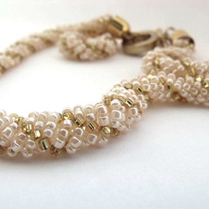 May include: A white and gold beaded necklace with a twisted design.