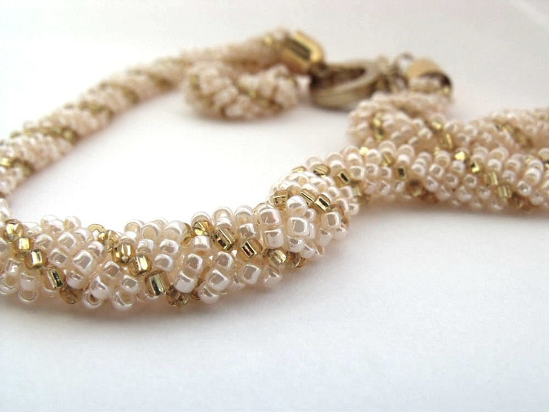 May include: A white and gold beaded necklace with a twisted design.