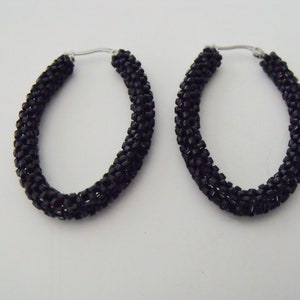 May include: A pair of black beaded hoop earrings. The earrings are made of small, black beads that are woven together to create a thick, oval shape.