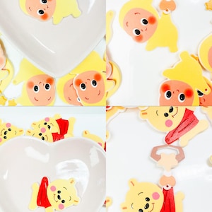 May include: A collage of images featuring heart-shaped dishes and yellow cartoon baby and bear-like figures with red scarves. The figures have smiling faces and are scattered around the dishes. The background is white.