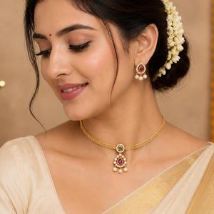 May include: A gold choker necklace featuring a central teardrop pendant with a red stone, a small green stone accent, and dangling white pearls. Matching gold stud earrings each feature a single red teardrop stone surrounded by small white pearls.