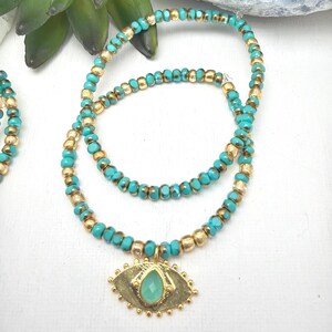 Puede incluir: Una pulsera de cuentas de doble hilo con cuentas alternas de color azul turquesa y oro metálico. La pulsera incluye un dije central en forma de ojo de tono dorado con una pequeña piedra de color verde claro en forma de lágrima.