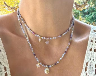 Peut inclure: Deux colliers de perles superposés avec de petites perles violet clair, roses et dorées. Le collier supérieur comporte un petit pendentif rose et un pendentif perle. Le collier inférieur a un petit pendentif en cristal et un plus grand pendentif perle.