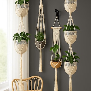 Può includere: Diverse fioriere sospese con piante verdi. Le fioriere sono color crema con un motivo floreale blu e bianco. Sono sospese da appendini in macramè bianco sporco. Una sedia intrecciata è in primo piano.