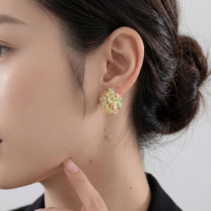 Peut inclure: Gros plan d'une boucle d'oreille à clou dorée ornée d'un amas de petites pierres d'opale iridescentes. La boucle d'oreille ronde est portée sur le lobe de l'oreille. L'arrière-plan est flou.