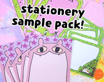 May include: A stationery sample pack featuring pink and green notepads with cartoon illustrations. The notepads have various designs, including a cat under a tree, a monster face, and a pink background with stars. The text "CRIMES" is visible on one notepad.