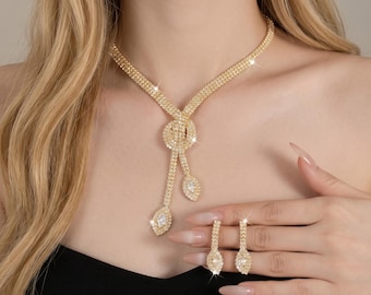 May include: A gold-coloured jewellery set featuring a necklace and earrings. The necklace has a knot design with dangling accents and a central pendant. The earrings are teardrop-shaped. The text "Midnight Luxe Jewelry" and "Feel the Love in Every Piece" is visible.