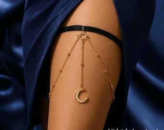 May include: A gold-coloured leg garter with a crescent moon pendant adorned with clear gemstones. The garter features a black velvet band and fine chain detailing. The image includes the text "Midnight Luxe Jewelry" and "Feel the Love in Every Piece".
