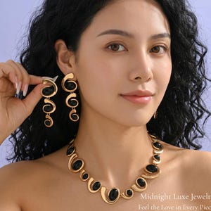 May include: Gold-toned jewelry set featuring a necklace and earrings with black oval accents. The necklace and earrings have a modern, abstract design. The image includes the text "Midnight Luxe Jewelry" and "Feel the Love in Every Piece".