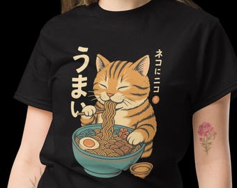 Puede incluir: Camiseta negra con un gato de dibujos animados comiendo ramen. El gato es naranja con rayas marrones. Texto japonés a la izquierda y a la derecha del gato. El ramen incluye fideos, un huevo y verduras.