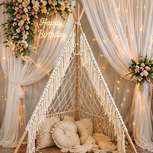 May include: A decorative teepee-style play tent with a macrame design, wooden poles, and a jute rug. The tent is filled with pillows and cushions. The words "Happy Birthday" are displayed on the wall. Floral arrangements and fairy lights add to the festive atmosphere.