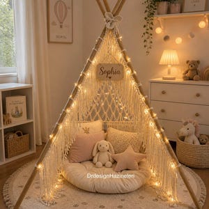 May include: A cozy, cream-colored teepee tent with string lights, a wooden frame, and macrame detailing. Inside are pillows, a stuffed bunny, and a star-shaped pillow. A wooden sign reads "Sophia". The tent sits on a round rug.