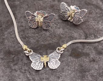May include: A silver butterfly necklace and matching earrings set. The jewelry features detailed butterfly pendants with silver wings and gold-colored bodies. The necklace has a delicate chain.