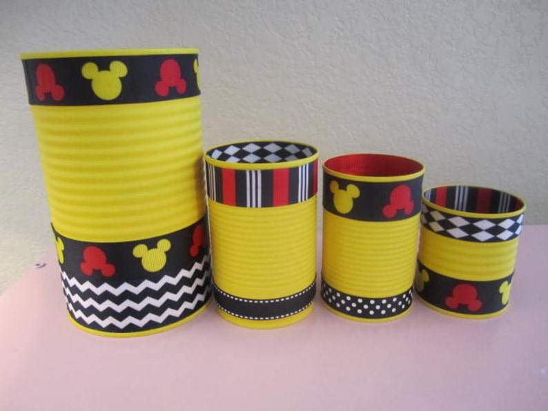K&ouml;nnte beinhalten: Vier gelbe zylindrische Beh&auml;lter mit schwarzem, rotem und wei&szlig;em gemustertem Band um die Oberseite. Die Beh&auml;lter sind mit Mickey-Maus-Ohren und -Gesichtern verziert.