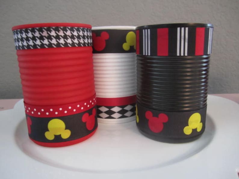May include: Three empty cans decorated with Mickey Mouse themed ribbon. The cans are red, white, and black. The ribbon features black and white houndstooth, red and white stripes, and black with red and yellow Mickey Mouse heads.