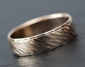 May include: A gold-colored ring with a textured, diagonal pattern around the band. The ring has a polished finish and a classic, rounded shape. The ring is likely made of metal and is designed for everyday wear.
