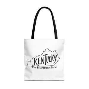 Può includere: Borsa tote bianca con manici neri. Presenta un contorno nero dello stato del Kentucky, con la parola "Kentucky" in un carattere scritto a mano e "The Bluegrass State" sotto.