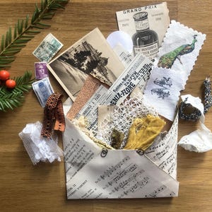 Könnte beinhalten: Eine Sammlung von Vintage-Ephemera, darunter Briefmarken, eine schwarz-weiße Postkarte, eine Pfauenillustration auf gewelltem Papier und Stoffreste, alles in einem handgefertigten Umschlag aus altem Notenblattpapier untergebracht.