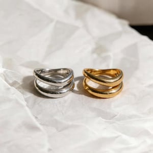 以下が含まれることがあります： 白くテクスチャ加工された表面に、銀色と金色の2つのリングが並んでいます。各リングは、滑らかで磨かれた仕上げのダブルバンドデザインが特徴です。リングは並んで配置されており、対照的な色と類似したスタイルを示しています。