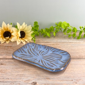May include: A rectangular ceramic tray featuring a mottled blue glaze with a dark brown, radiating leaf-like pattern etched into the surface. The tray has slightly raised edges and a glossy finish, showcasing a handcrafted appearance.