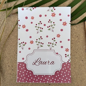 Könnte beinhalten: Eine weiße Karte mit floralem Design und dem Namen "Laura" in Schreibschrift. Die obere Hälfte zeigt rosa Blumen und Beeren mit rosa Tupfen. Die untere Hälfte hat ein rosa Tupfenmuster.
