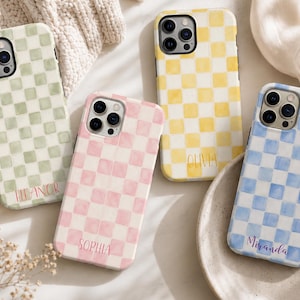May include: Four phone cases with a watercolor checkerboard pattern in pastel colors: green, pink, yellow, and blue. Each case has a name printed on it: Eleanor, Sophia, Olivia, and Miranda. The cases are on a white surface.