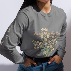May include: Gray long-sleeve shirt with the text "Texas Strong" on the left sleeve and "Stronger than the Storm" with a floral design on the front. The floral design includes white, yellow, and blue flowers.