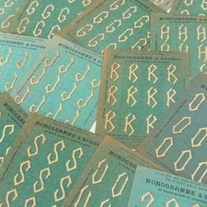 Op de afbeelding: Een verzameling vintage monogramkaarten met letters zoals G, B en S. De kaarten hebben een turquoise achtergrond met een rasterpatroon en de Franse tekst "MONOGRAMME à broder". De letters zijn crèmekleurig.