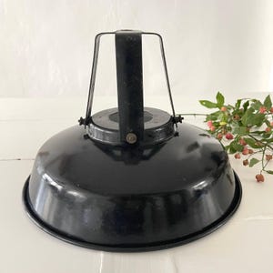May include: A black, industrial-style pendant light fixture with a rounded shade and a metal handle. The shade has a glossy finish. The fixture is designed for overhead lighting and is suitable for various interior design styles.